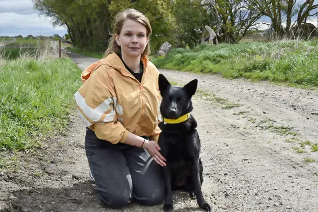 En person sitter på en grusväg med en hund. Foto.